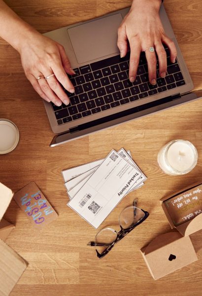 Overhead Shot Of Woman Running Online Business Making Boutique Candles At Home Working On Laptop
