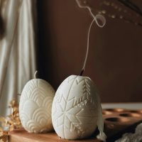 Traditional Easter decor. Burning soy candles in the shape of white eggs on a brown textured backgro